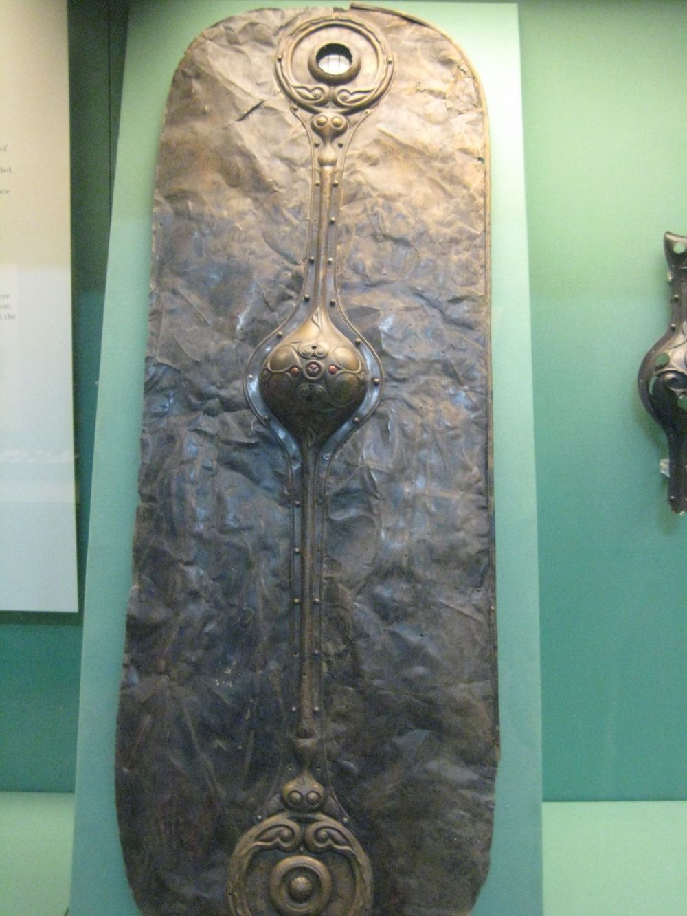 Revêtement de bouclier en bronze martelé, long et étroit, avec umbo central, exposé en vitrine